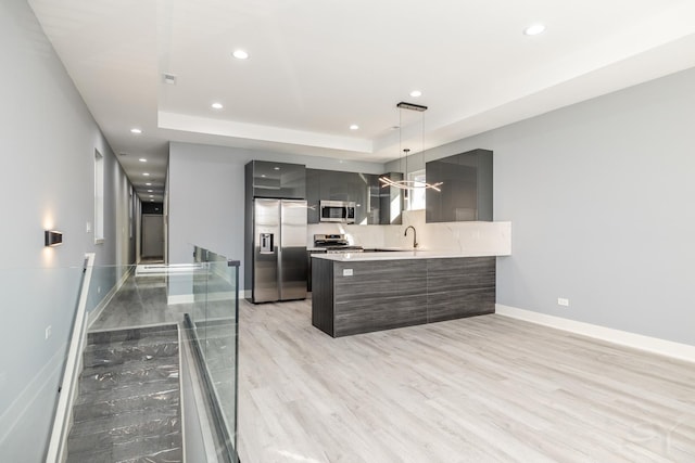 kitchen with stainless steel appliances, kitchen peninsula, a tray ceiling, sink, and decorative light fixtures