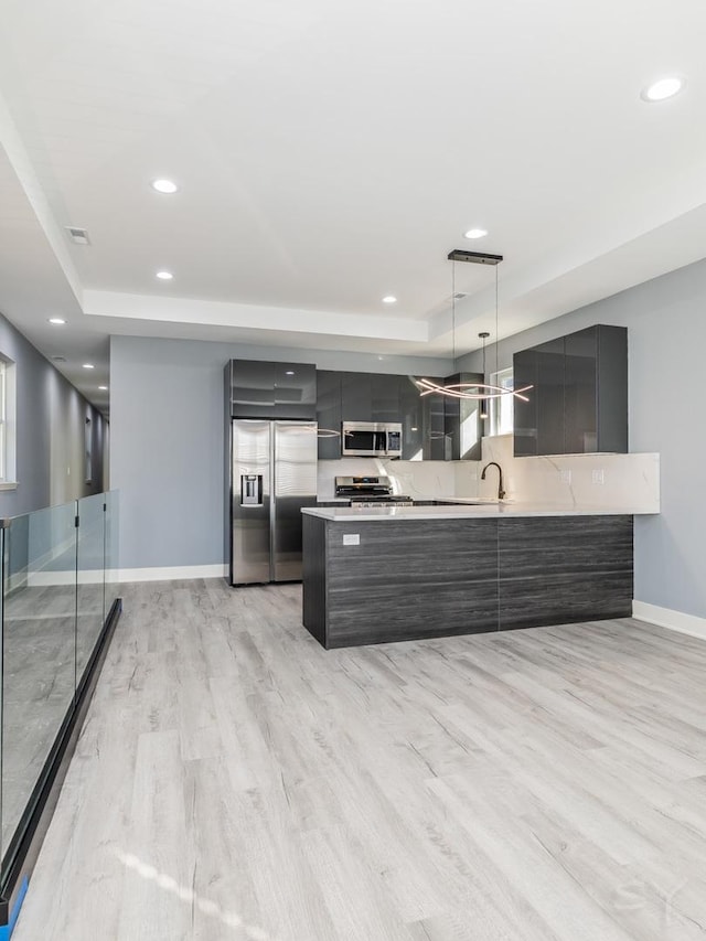 kitchen featuring appliances with stainless steel finishes, decorative light fixtures, kitchen peninsula, and a tray ceiling