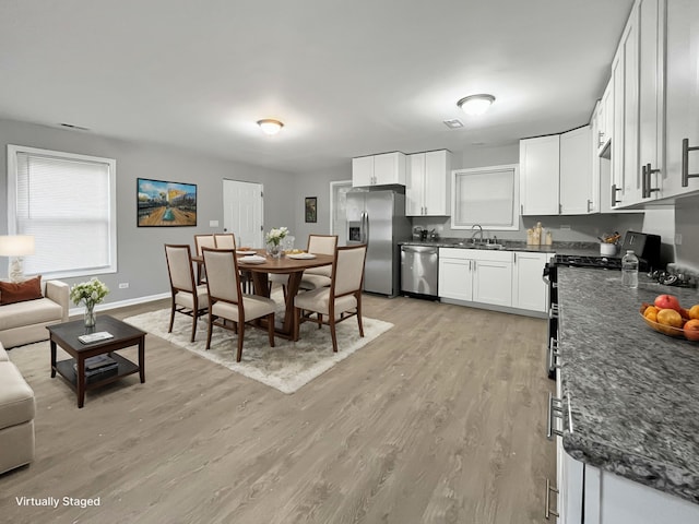 kitchen with light hardwood / wood-style flooring, white cabinets, dark stone counters, appliances with stainless steel finishes, and sink