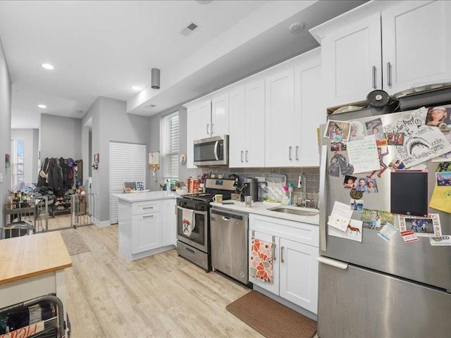 kitchen with white cabinets, stainless steel appliances, tasteful backsplash, sink, and light wood-type flooring