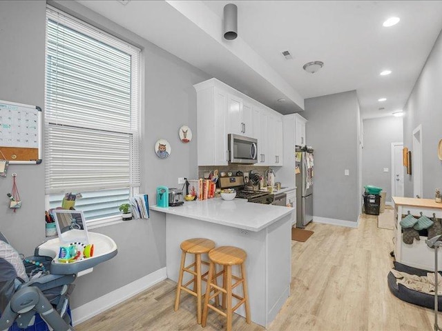 kitchen featuring light hardwood / wood-style floors, kitchen peninsula, a kitchen bar, stainless steel appliances, and white cabinets