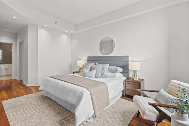 bedroom with ensuite bathroom, wood-type flooring, and a tray ceiling