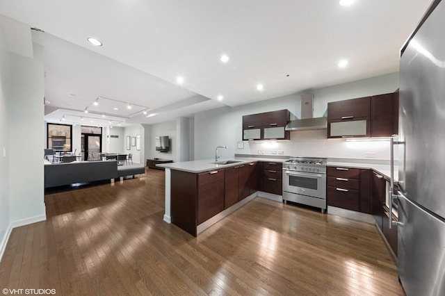 kitchen with appliances with stainless steel finishes, dark hardwood / wood-style flooring, wall chimney range hood, dark brown cabinetry, and sink