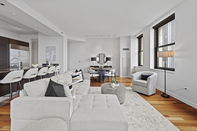 living room with rail lighting, sink, and light hardwood / wood-style flooring