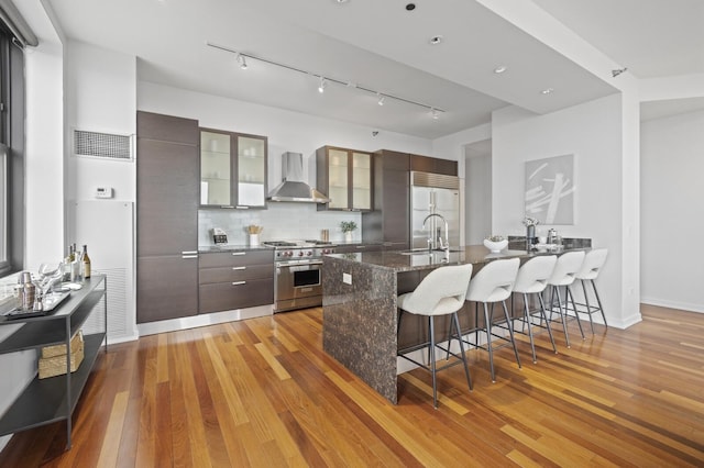 kitchen with decorative backsplash, sink, premium appliances, a breakfast bar area, and wall chimney exhaust hood