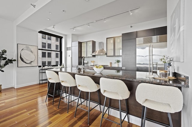 kitchen with appliances with stainless steel finishes, wall chimney exhaust hood, decorative backsplash, sink, and a kitchen breakfast bar