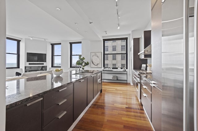 kitchen featuring stainless steel range, track lighting, dark stone countertops, refrigerator, and light hardwood / wood-style flooring