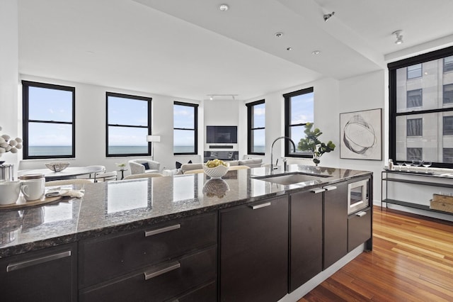 kitchen featuring stainless steel microwave, wood-type flooring, dark stone counters, and sink