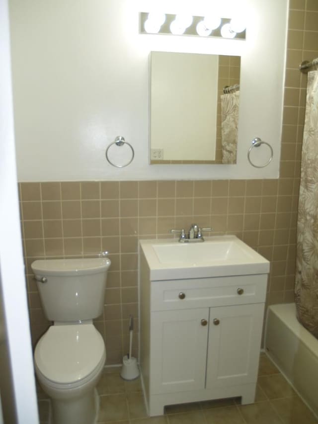 full bathroom featuring toilet, tile patterned floors, vanity, and tile walls