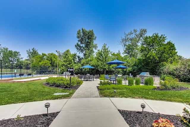 view of property's community featuring a lawn, tennis court, and a patio area