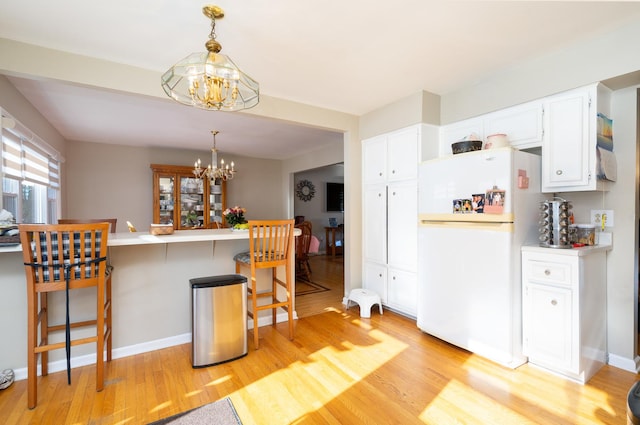 kitchen with a chandelier, pendant lighting, white refrigerator, a kitchen bar, and white cabinetry