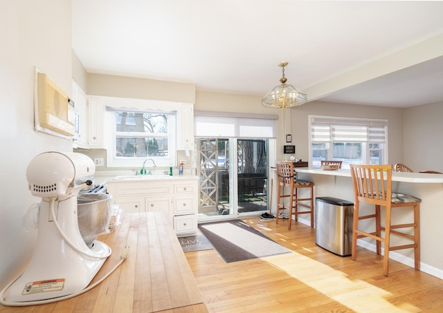 kitchen featuring light hardwood / wood-style flooring, decorative light fixtures, white cabinetry, a breakfast bar area, and sink