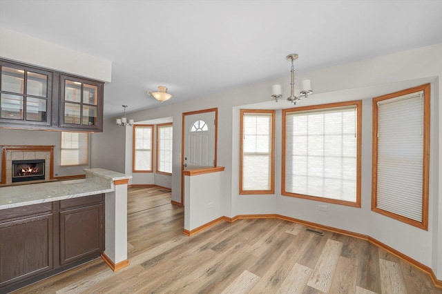 kitchen with light hardwood / wood-style floors, a tiled fireplace, a notable chandelier, dark brown cabinets, and pendant lighting