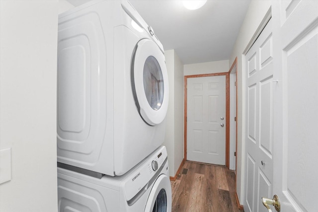 clothes washing area featuring stacked washing maching and dryer and dark hardwood / wood-style flooring