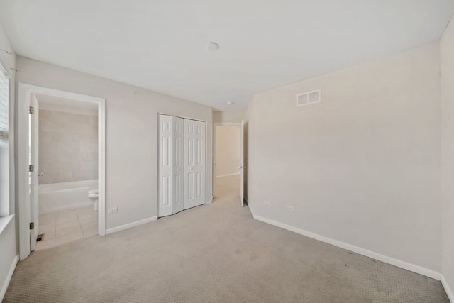 unfurnished bedroom featuring ensuite bathroom, a closet, and light colored carpet