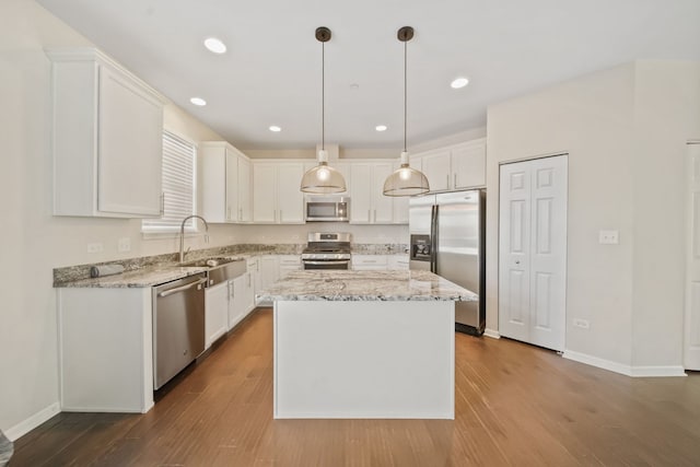 kitchen with stainless steel appliances, a kitchen island, sink, white cabinetry, and decorative light fixtures