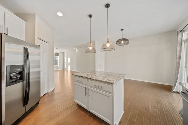 kitchen with white cabinets, stainless steel fridge, decorative light fixtures, and light stone counters