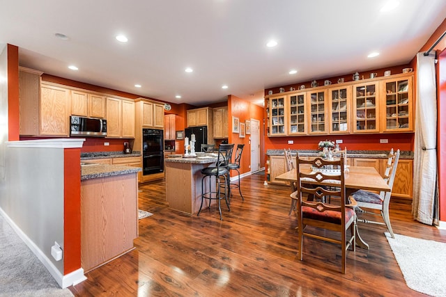 kitchen with dark wood-type flooring, a breakfast bar, dark stone countertops, a kitchen island, and black appliances