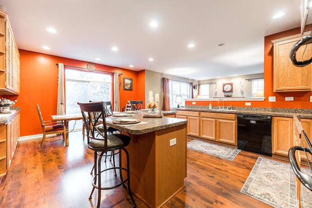 kitchen featuring dark hardwood / wood-style flooring, sink, a center island, a breakfast bar, and black dishwasher