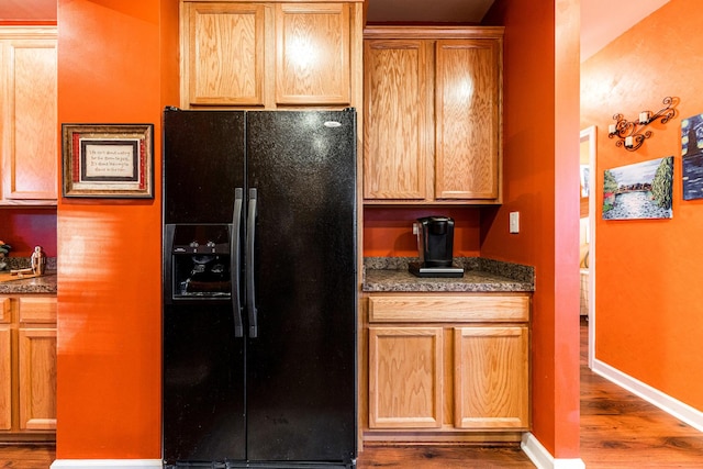 kitchen featuring dark stone countertops, light hardwood / wood-style flooring, and black fridge with ice dispenser