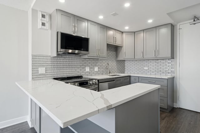 kitchen featuring kitchen peninsula, appliances with stainless steel finishes, light stone countertops, and gray cabinetry