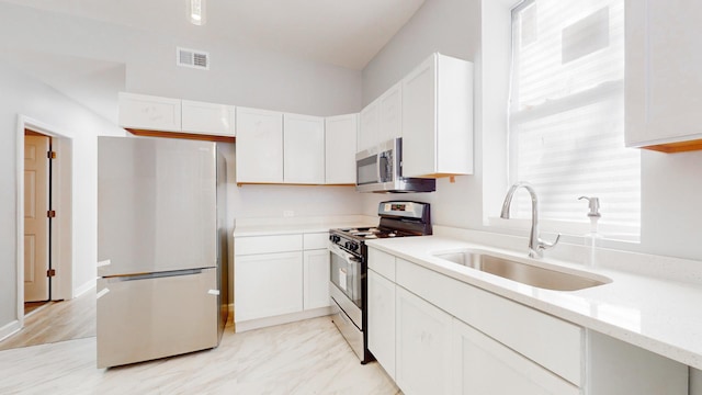 kitchen with light stone counters, sink, white cabinets, and stainless steel appliances