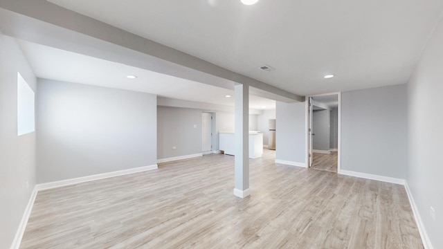 basement featuring stainless steel fridge and light hardwood / wood-style flooring