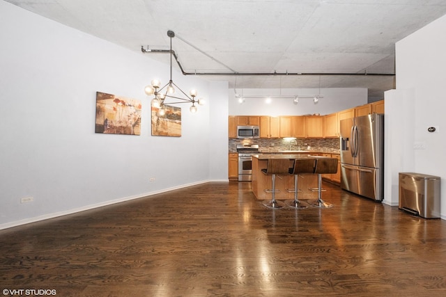 kitchen featuring dark wood-style flooring, decorative light fixtures, appliances with stainless steel finishes, a kitchen island, and a kitchen bar