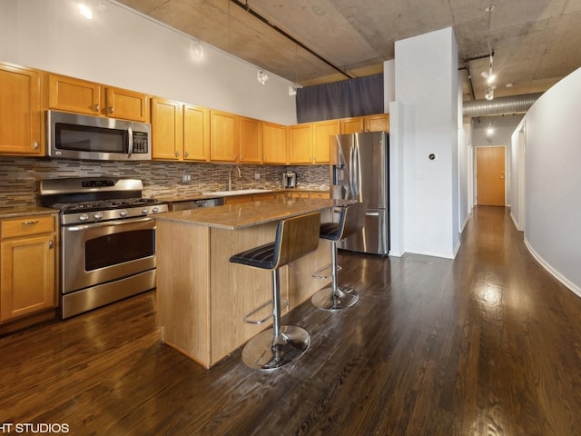 kitchen with a breakfast bar area, dark wood-type flooring, a sink, a kitchen island, and appliances with stainless steel finishes