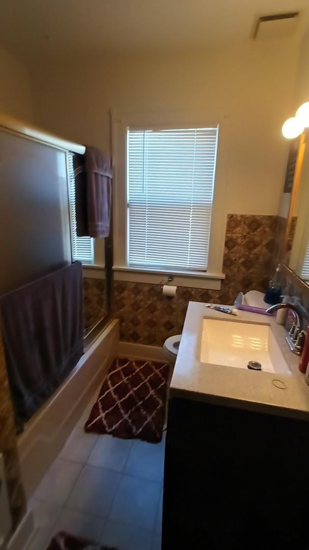 full bathroom featuring toilet, vanity, tile patterned floors, and combined bath / shower with glass door