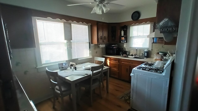 kitchen with sink, wall chimney exhaust hood, hardwood / wood-style floors, ceiling fan, and gas range gas stove