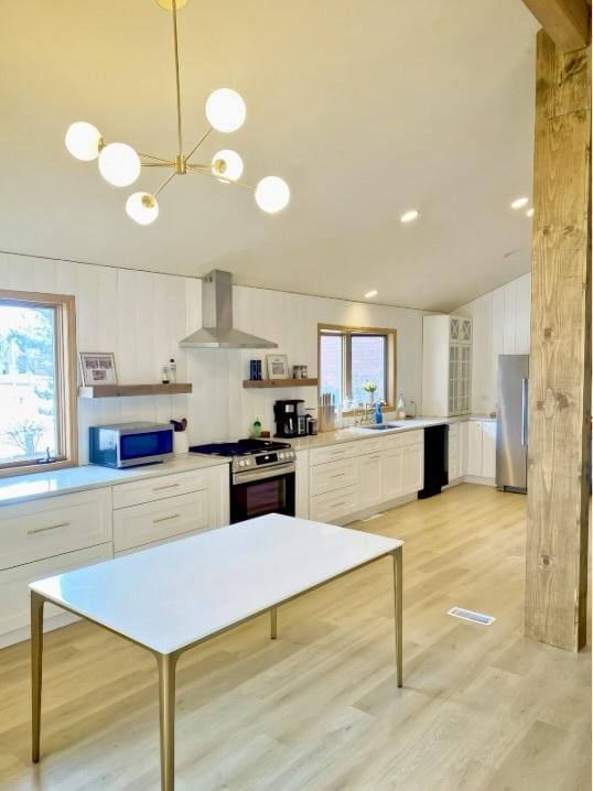 kitchen with stainless steel appliances, hanging light fixtures, wall chimney range hood, and white cabinets