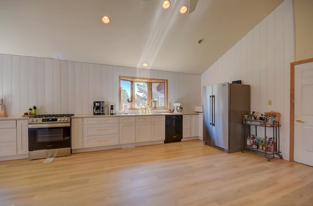 kitchen with sink, wood walls, light wood-type flooring, appliances with stainless steel finishes, and white cabinets