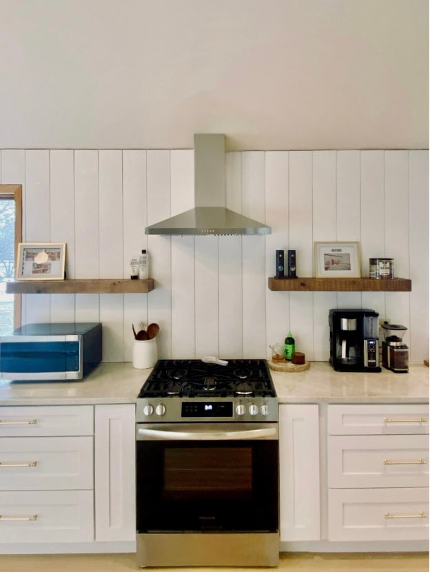 kitchen featuring appliances with stainless steel finishes, white cabinets, backsplash, light stone counters, and wall chimney range hood