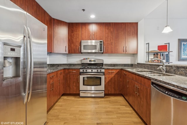 kitchen featuring appliances with stainless steel finishes, sink, dark stone countertops, hanging light fixtures, and light hardwood / wood-style flooring