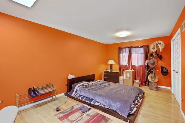 bedroom with a skylight, visible vents, baseboards, and wood finished floors