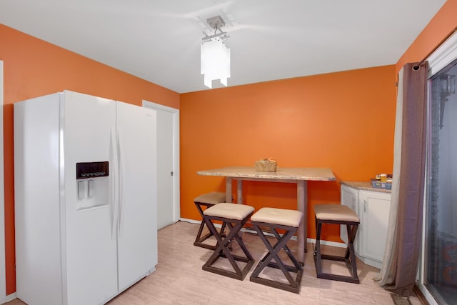 kitchen with white fridge with ice dispenser, light countertops, and white cabinets