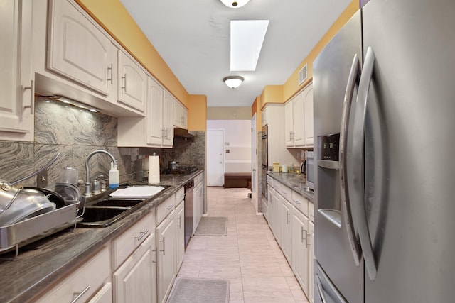 kitchen with stainless steel appliances, dark countertops, tasteful backsplash, visible vents, and a sink