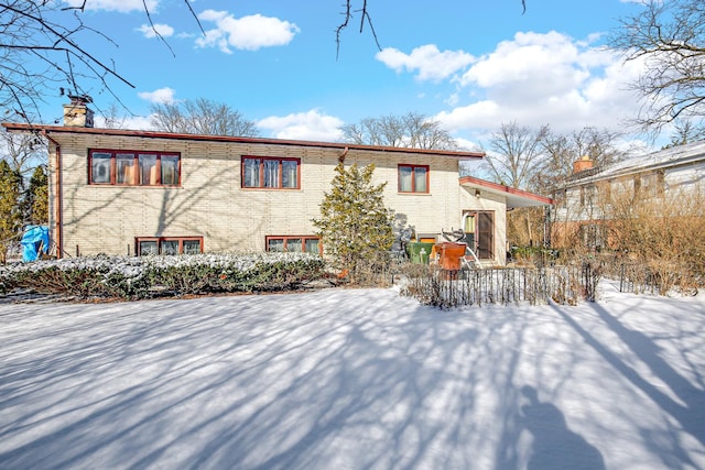 snow covered property with brick siding and a chimney