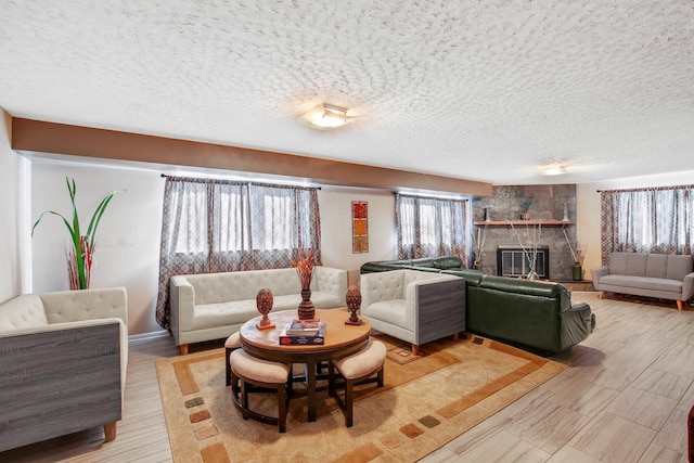 living room with light wood finished floors, a textured ceiling, and a stone fireplace