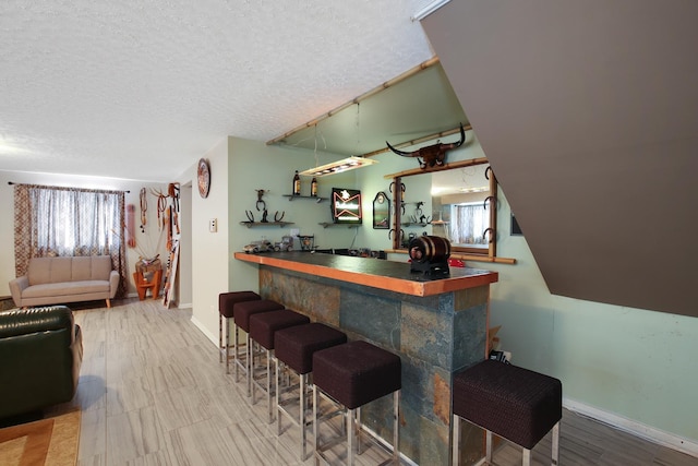 bar with a wealth of natural light, baseboards, a textured ceiling, and a bar