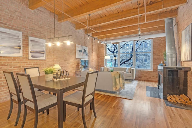 dining space with wood ceiling, hardwood / wood-style floors, brick wall, beamed ceiling, and a wood stove