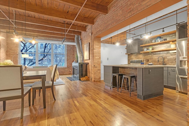 dining room with a wood stove, wood ceiling, light hardwood / wood-style floors, and brick wall