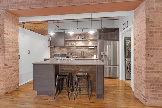 bar with wall chimney range hood, hardwood / wood-style flooring, hanging light fixtures, stacked washer / drying machine, and stainless steel fridge with ice dispenser