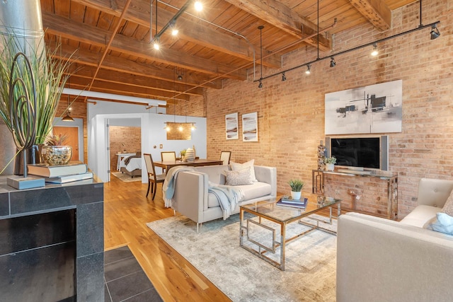 living room with wood ceiling, beam ceiling, a towering ceiling, wood-type flooring, and brick wall