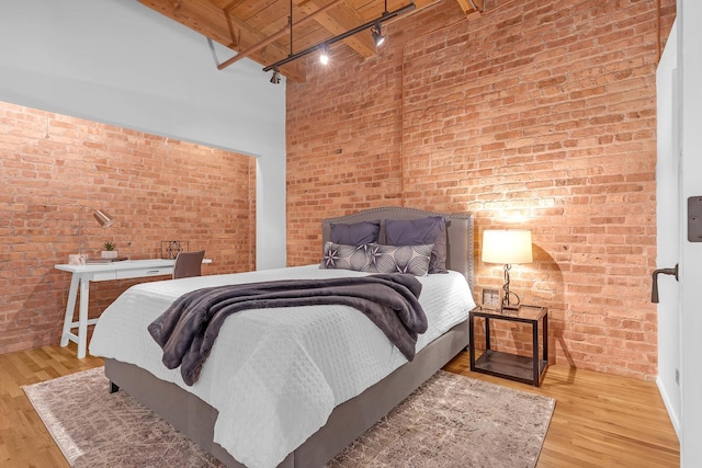 bedroom featuring brick wall, a towering ceiling, and light wood-type flooring