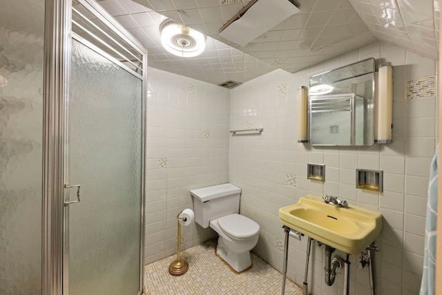 bathroom featuring tile patterned flooring, a shower with door, sink, tile walls, and toilet