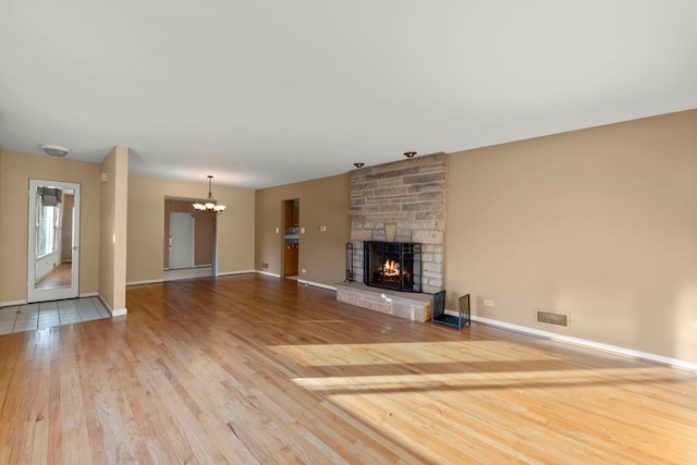 unfurnished living room with light hardwood / wood-style flooring, a stone fireplace, and a notable chandelier