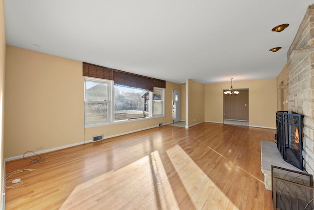 unfurnished living room with a notable chandelier, a stone fireplace, and light hardwood / wood-style flooring