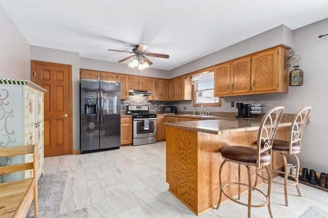 kitchen with kitchen peninsula, decorative backsplash, a kitchen bar, appliances with stainless steel finishes, and ceiling fan